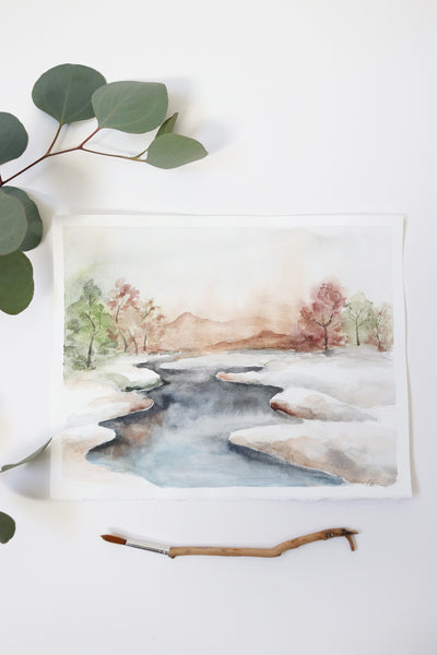 icy stream divides watercolor landscape into two snowy fields flat lay