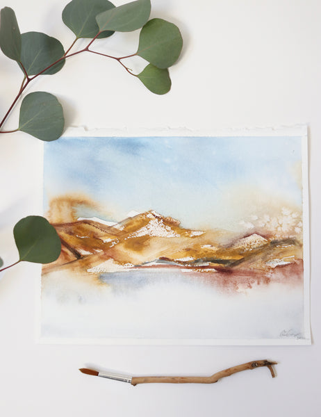 Rich earth-tone washes of color reveal a desert hill watercolor landscape flat lay